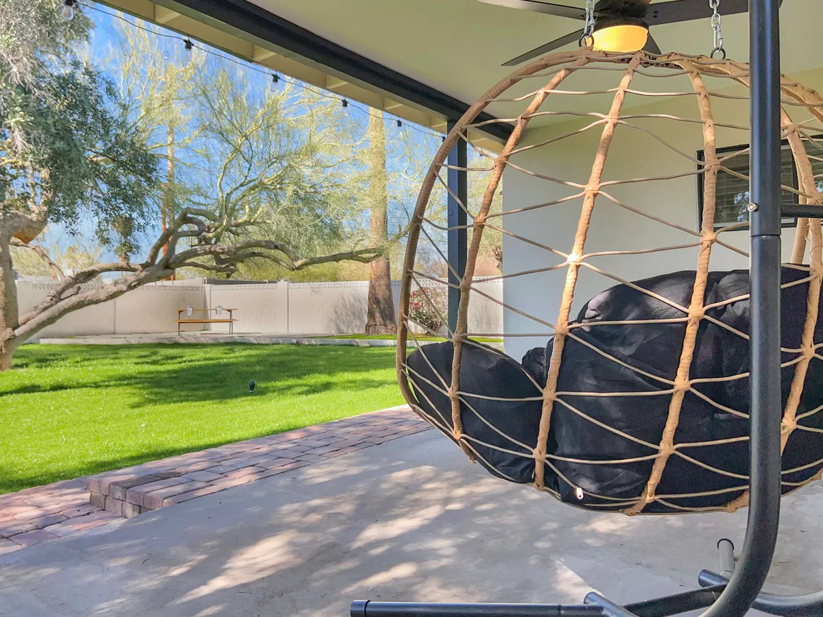 A tranquil backyard scene featuring a hanging chair nestled beneath the shade of mature tree branches, with a lush green lawn stretching out and dappled sunlight filtering through the leaves. The space radiates serenity and an inviting connection to nature, perfect for quiet relaxation after outdoor adventures.