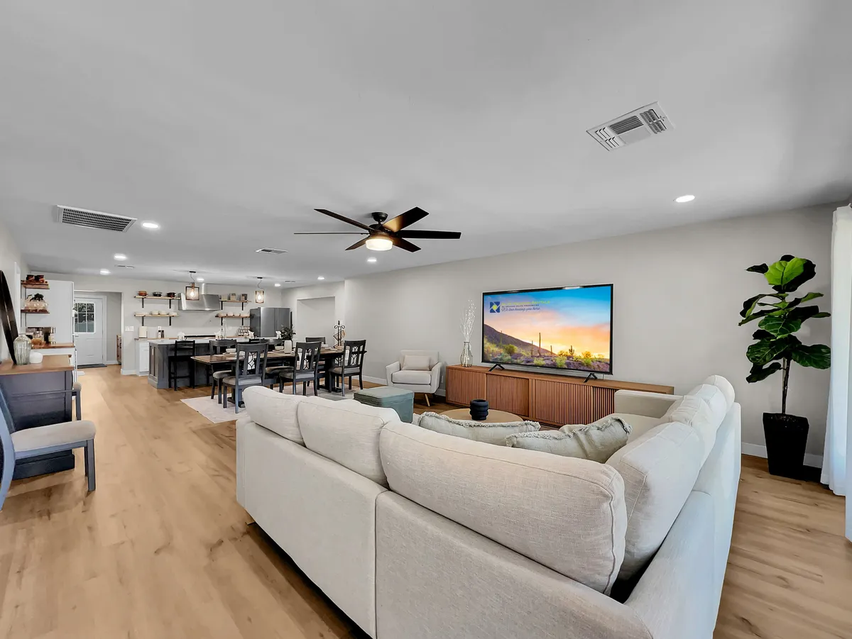 This image showcases a comfortable living area featuring a plush sofa oriented toward a television, with a dining space visible in the background. The open-concept layout allows for easy movement and interaction between the living and dining zones, evoking a sense of togetherness ideal for family gatherings or movie nights.