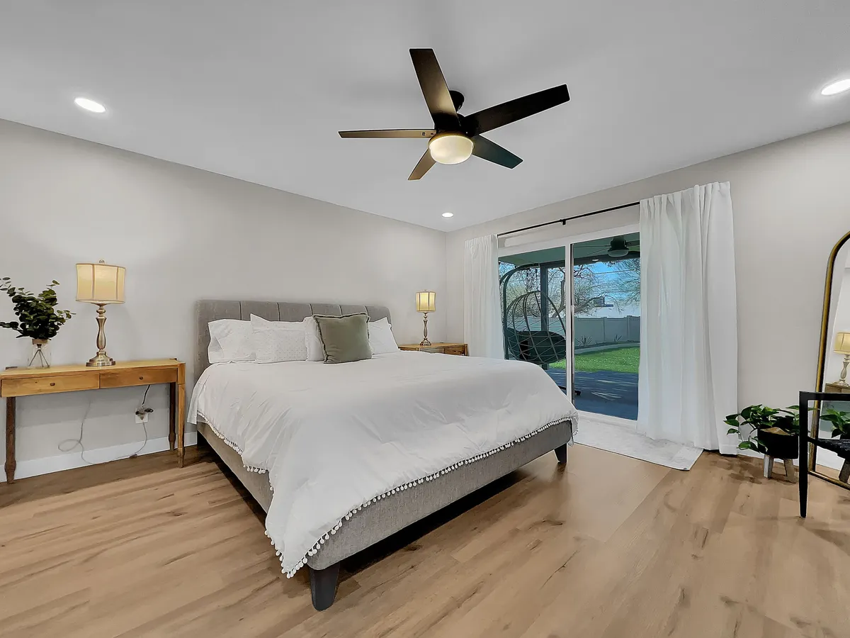 A serene bedroom with a large bed dressed in crisp white linens, wooden bedside tables, and a sliding glass door that opens to a view outside. Natural light fills the room, enhancing the sense of tranquility and modern comfort.