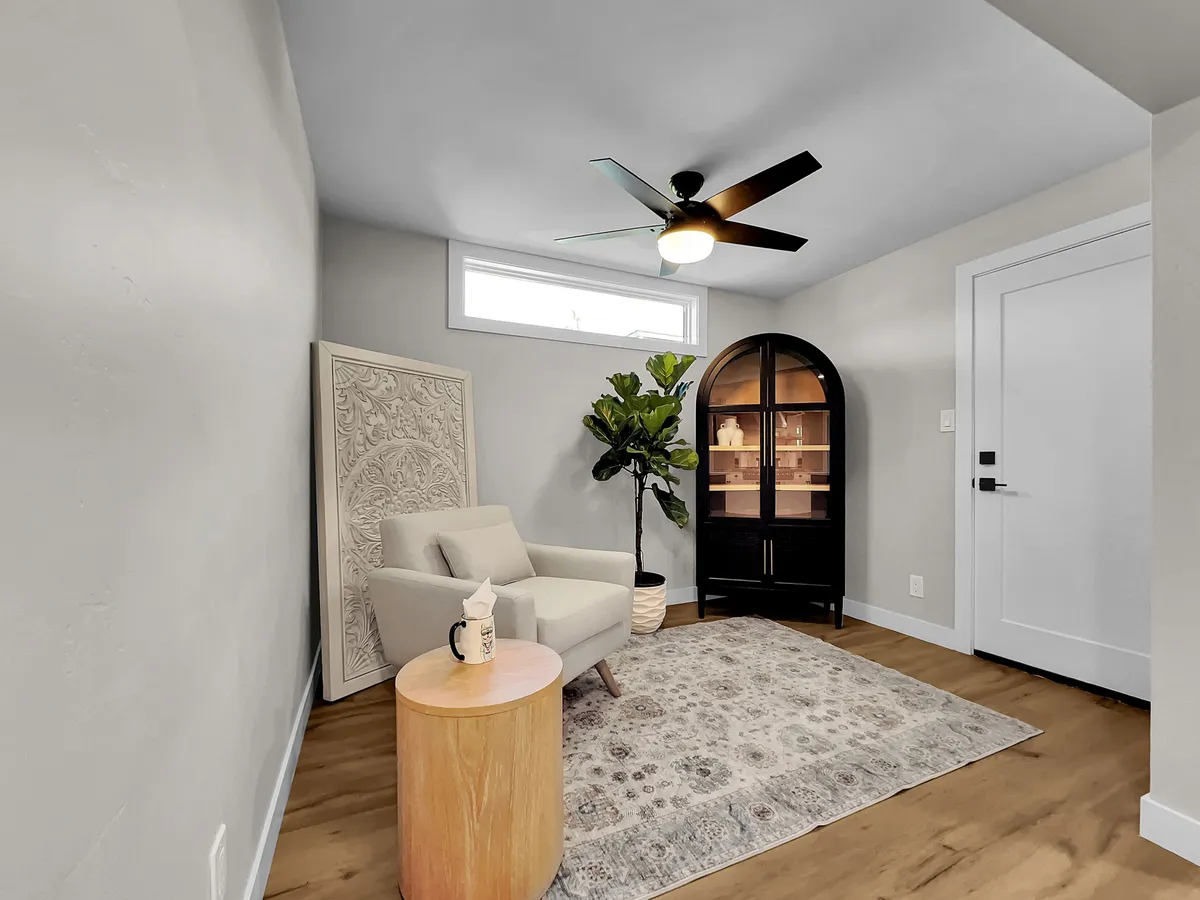 A cozy corner with a comfortable armchair, decorative area rug, tall plant, and curved display cabinet bathed in natural light. The scene is inviting and restful, perfect for unwinding after a day of work or exploring the city.