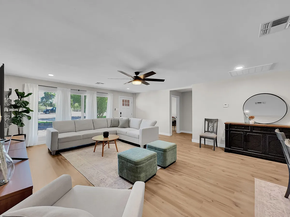 A bright, open living area with a light-colored sectional sofa, round coffee table, green ottomans, large curtained windows, and a decorative mirror. The space feels airy and cozy—ideal for relaxing after arrival or preparing for city adventures.
