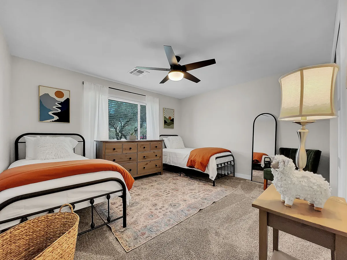 A cozy bedroom with two twin beds accented by orange details, a wooden dresser, decorative artwork on the walls, and a floor lamp. The warm, welcoming atmosphere is suited for restful evenings and gentle morning wakeups.