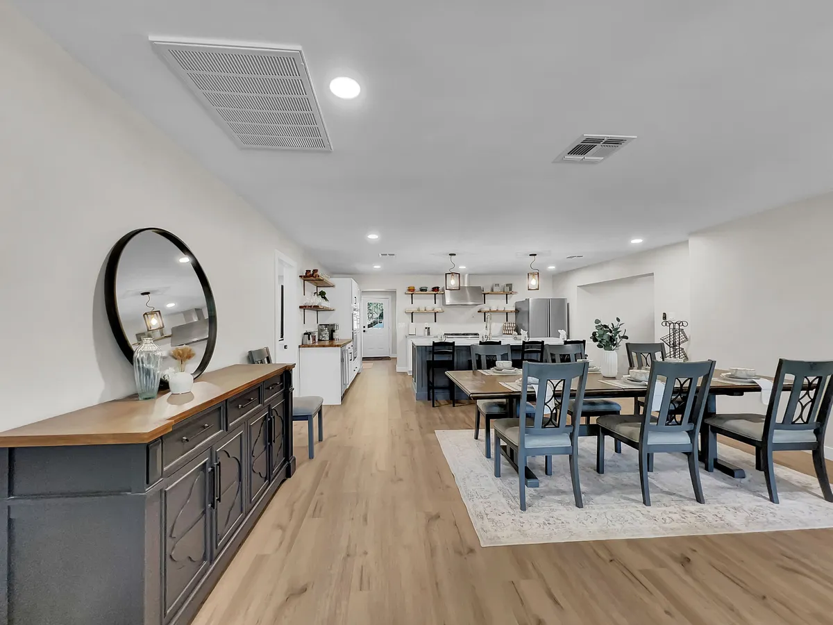A welcoming open-plan dining area featuring a large dining table, a stylish kitchen island, and a decorative wall mirror. The space is designed for gatherings, with comfortable seating and warm lighting that sets the stage for memorable meals and socializing.