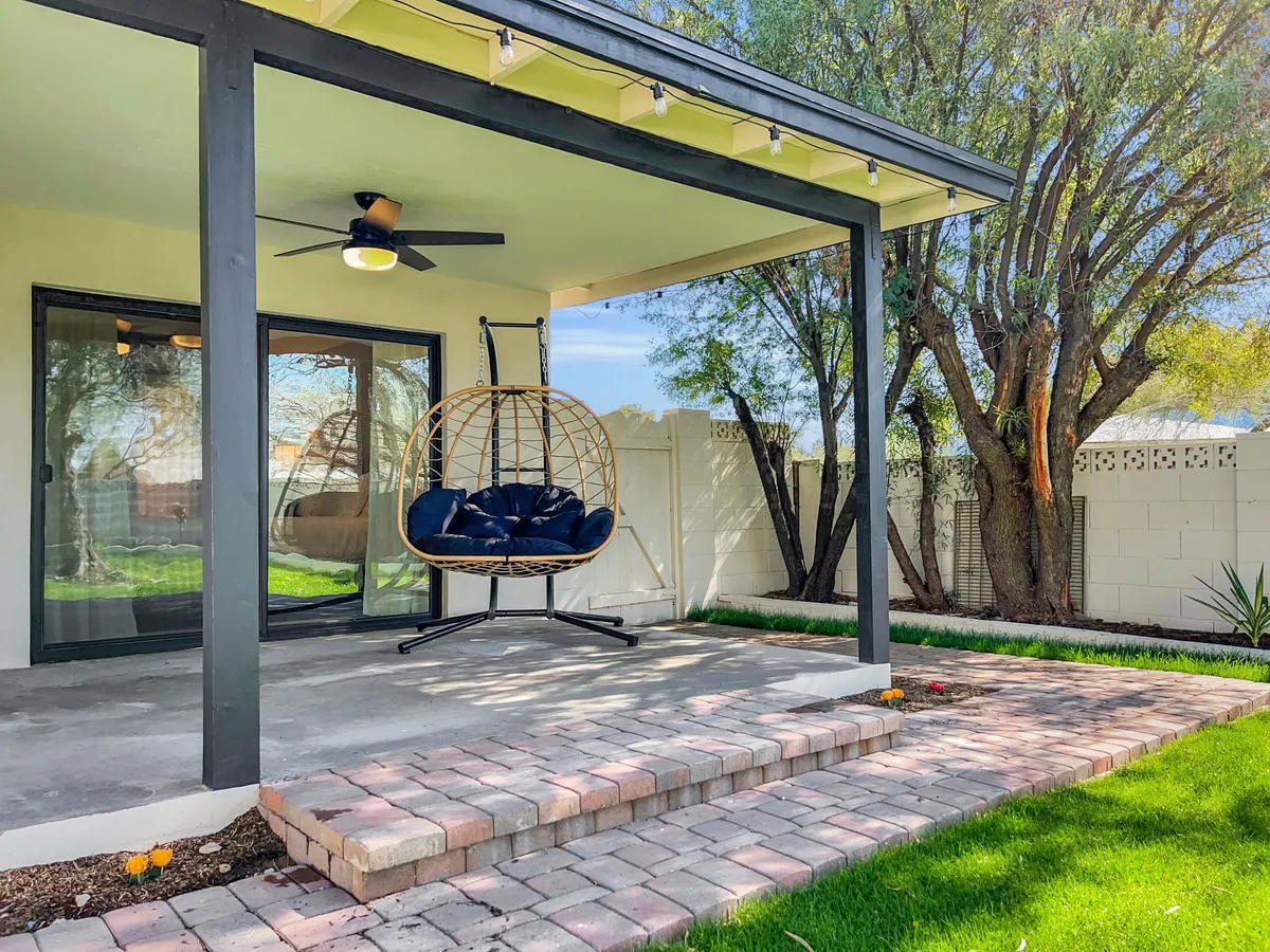This view centers on a cozy patio area with a stylish hanging chair overlooking a well-maintained green lawn. The setup invites guests to relax outdoors, read, or enjoy the warm Arizona breeze while staying connected to the backyard's natural beauty.
