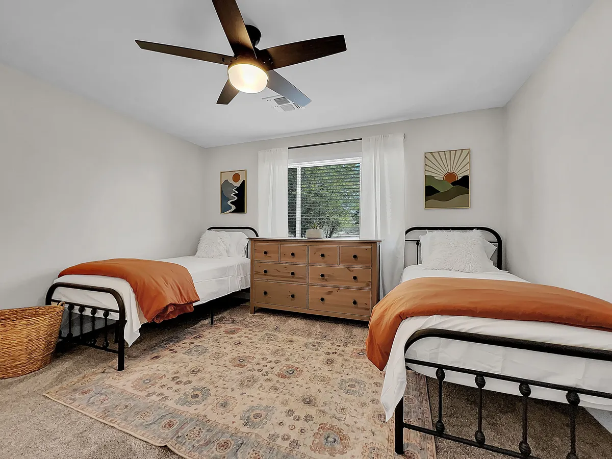 A cheerful bedroom with two twin beds, a dresser, soft window light, curtains, and playful artwork. The cozy, inviting atmosphere is perfect for families with children or friends traveling together, supporting restful nights after busy days exploring the neighborhood park and local attractions.