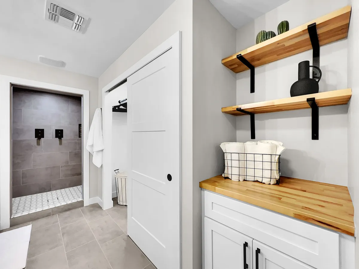 A calm, inviting bathroom with a beautifully tiled shower area, shelves adorned with tasteful décor, and a wooden countertop. The space evokes a sense of tranquility and is oriented toward relaxation and morning rituals.