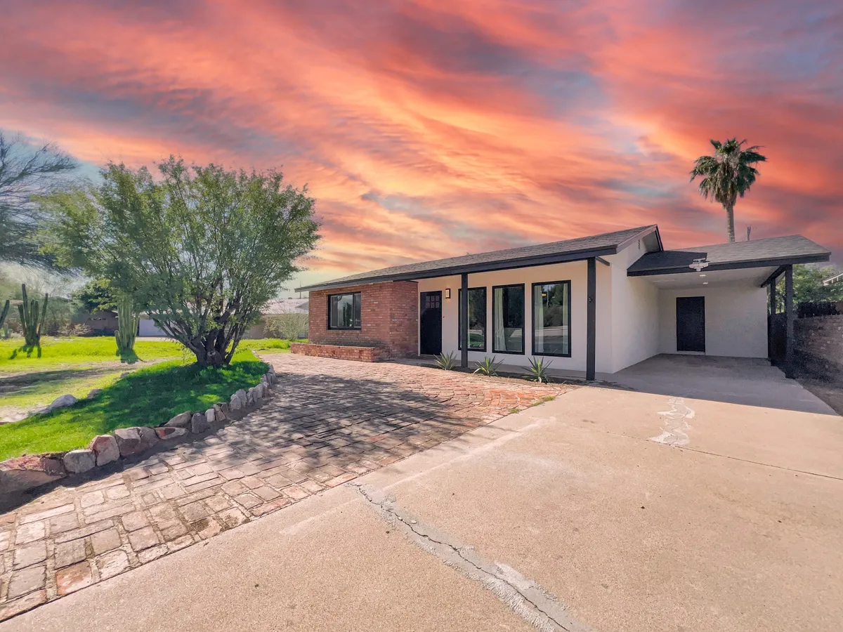 A visually striking exterior view of the home at sunset, highlighting modern architectural lines, a lush landscaped garden, and a paved driveway. The vibrant sky hints at the beauty of Arizona evenings, while the outdoor area suggests opportunities for gatherings, relaxation, and enjoying the garden.