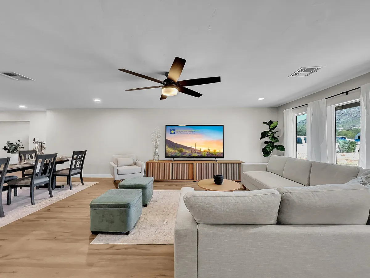 A welcoming living space with a large, comfortable sectional sofa, a coffee table, and a television, all adjacent to a dining table. The setup suggests both casual and festive occasions, from movie nights to intimate dinners, and captures the inclusive feel of the space.