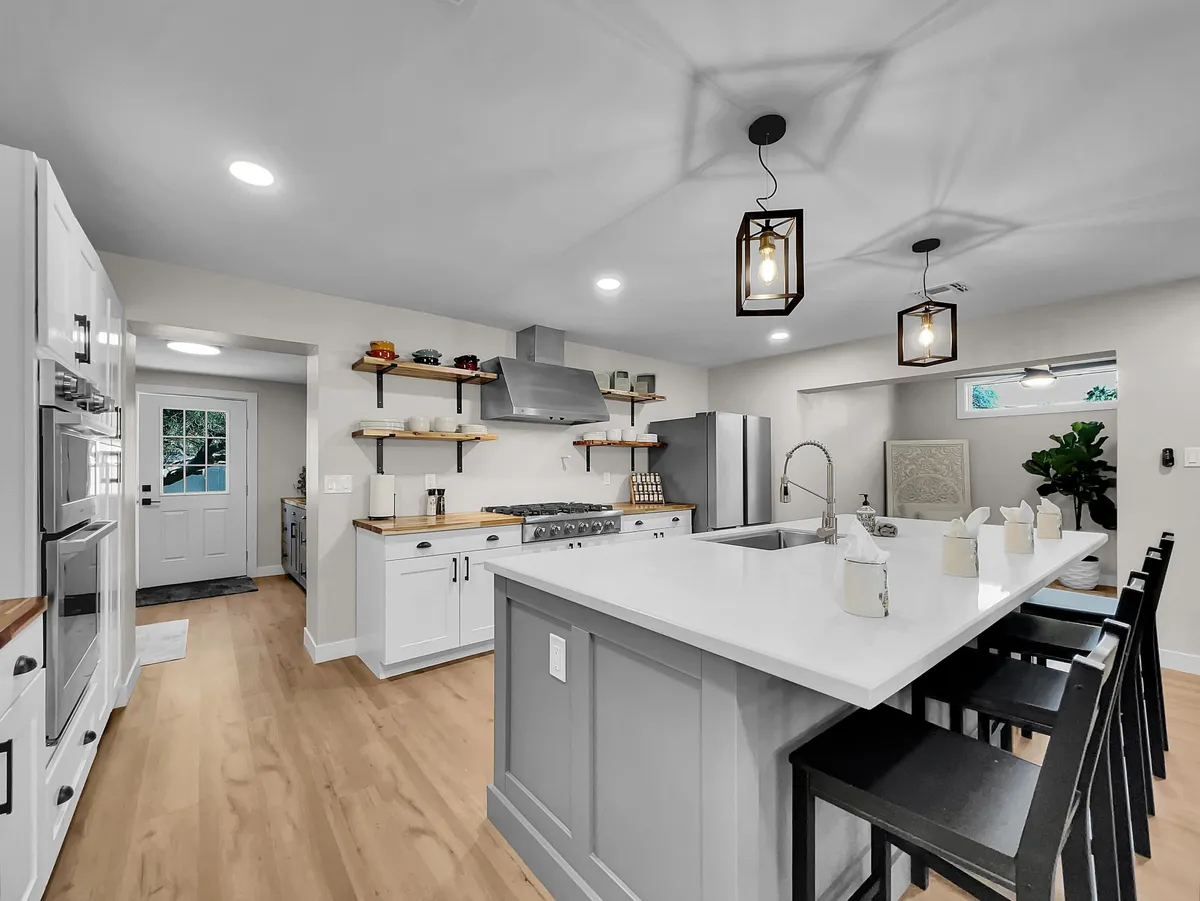 A bright, open kitchen featuring a spacious island, stainless steel appliances, open shelving, and pendant lights. The layout is designed for social cooking and group gatherings, with plenty of room for multiple people to participate in meal preparation. The inviting ambiance encourages interaction and sharing memorable moments.