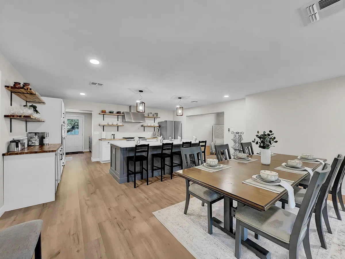 An inviting kitchen and dining area with a large dining table, kitchen island, open shelving, and modern pendant lights. The open design encourages shared cooking experiences and casual conversation, reflecting the 'gourmet kitchen' and 'gathering' themes of the section.